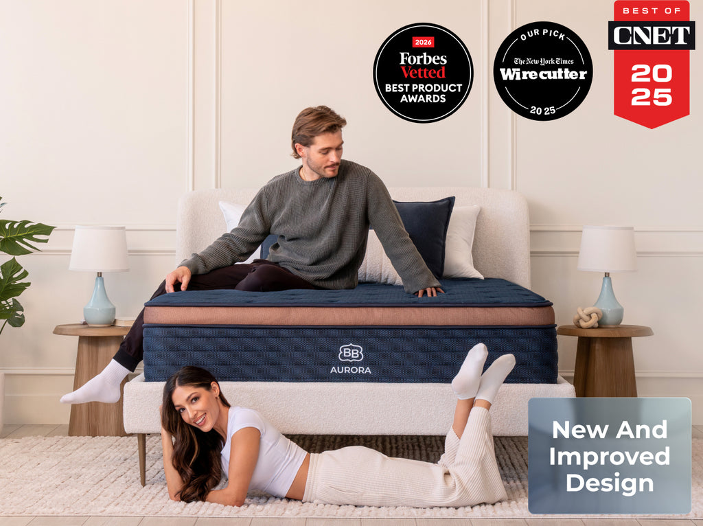 Two adults pose with the Brooklyn Bedding Aurora Luxe Cooling mattress in a bright bedroom with award badges above.