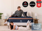 Two adults pose with the Brooklyn Bedding Aurora Luxe Cooling mattress in a bright bedroom with award badges above.